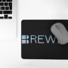 Black Brewer Mouse Pad with grey mouse on top next to laptop