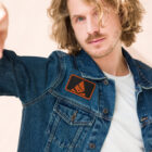 Man wearing jean jacket with embroidered Bank of Zaonce logo in orange